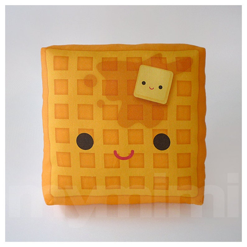 May include: A yellow waffle pillow with a smiling face and a small yellow square of butter on top. The pillow is made of soft fabric and has a waffle pattern.