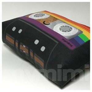 May include: A black and brown cassette tape pillow with a rainbow design. The tape has a purple and brown label with the text "mymimimi" printed on it.