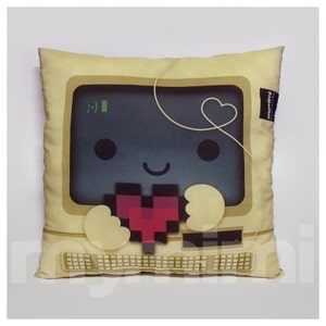 May include: A beige pillow with a computer screen design. The computer screen has a pixelated heart and a smiling face. The pillow has a white cord with a heart at the end.
