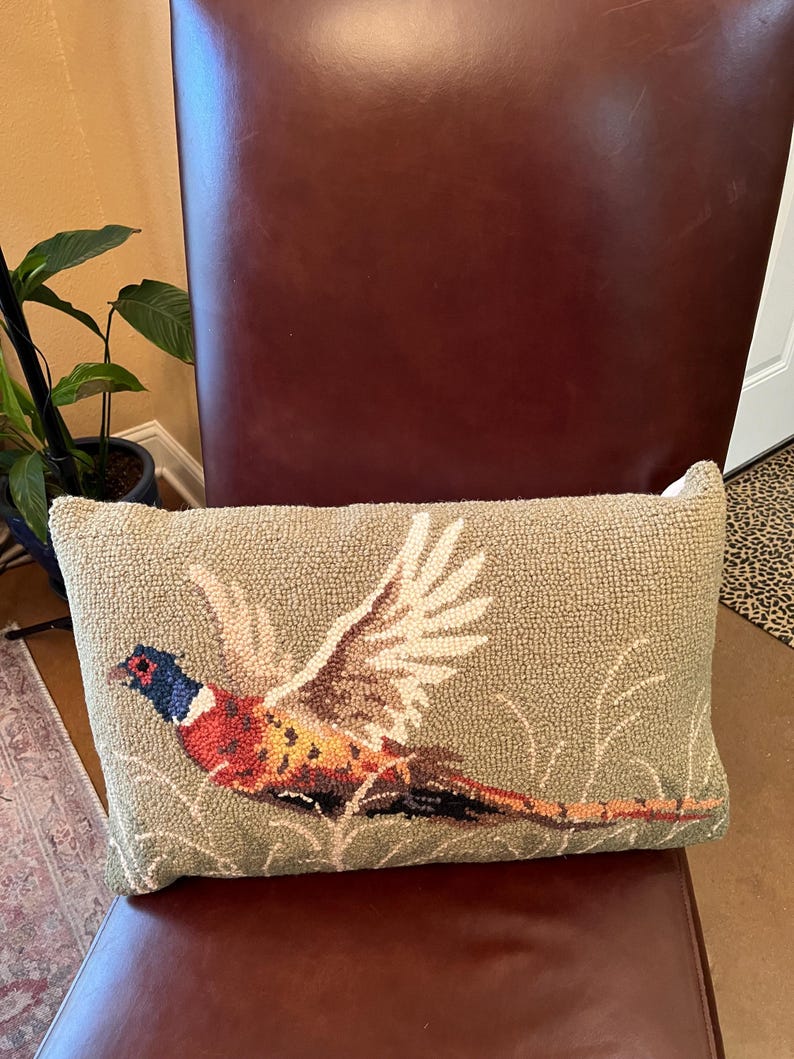 May include: A green throw pillow with a needlepoint design of a pheasant in flight. The pheasant is brown, orange, and blue with white wings.