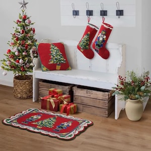 May include: A festive Christmas scene featuring a decorated tree, red stockings, a pillow, and a rug. The rug and pillow have a Christmas tree design. Presents wrapped in gold and red ribbon are under the bench. A vase of greenery sits on the right.