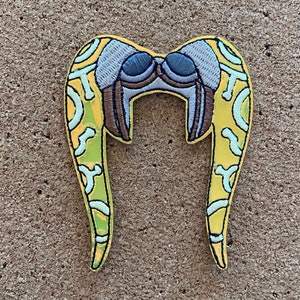 May include: Yellow embroidered patch with a pair of horns, resembling a headdress. The horns have a light blue and white pattern and a brown detail in the center.