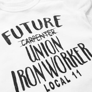 May include: White t-shirt with black text that reads "FUTURE CARPENTER UNION IRON WORKER LOCAL 11". The word "CARPENTER" is crossed out.