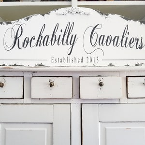 May include: White painted cabinet with a sign that reads "Rockabilly Cavaliers - Established 2013".