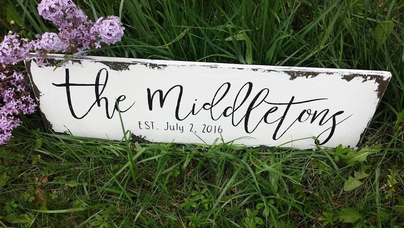May include: White wooden sign with black painted text that reads "The Middletons Est. July 2, 2016". The sign is distressed and has a rustic look.
