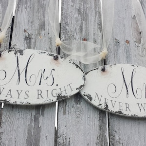 May include: Two white oval signs with black lettering hanging on a weathered wooden fence. The signs read "Mrs. Always Right" and "Mrs. Never Wrong".