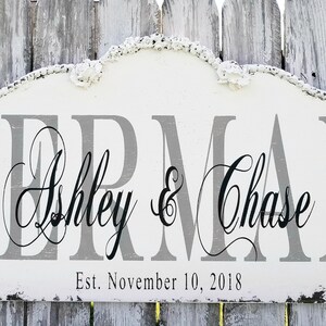 Puede incluir: Un letrero de madera blanco con un acabado de pintura gris desgastado. El letrero tiene una parte superior curva y dice "Berman Ashley & Chase Est. November 10, 2018".