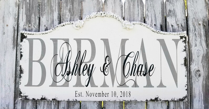 Puede incluir: Un letrero de madera blanco con un acabado de pintura gris desgastado. El letrero tiene una parte superior curva y dice "Berman Ashley & Chase Est. November 10, 2018".