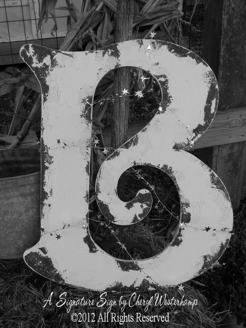 May include: A white wooden letter B with a distressed finish. The letter is decorated with a string of silver stars. The letter is sitting on a bed of brown leaves and twigs. The text "A Signature Sign by Cheryl Westerkamp &copy;2012 All Rights Reserved" is printed below the letter.