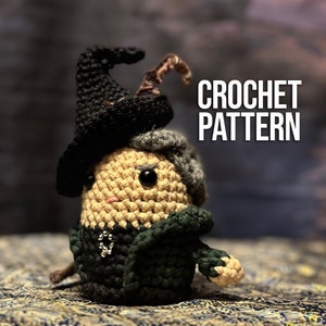 May include: Crochet pattern for a small, amigurumi-style witch doll. The doll is wearing a black hat, a green robe, and has a white beard. The doll has black eyes and a pink nose.