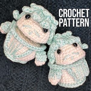Puede incluir: Dos juguetes amigurumi tejidos a crochet con hilo de color azul claro y blanco. Los juguetes tienen un cuerpo redondo y una cara con ojos y boca. El texto "CROCHET PATTERN" está en el fondo.