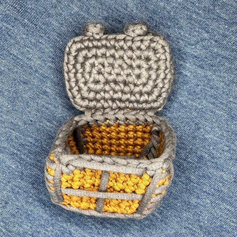 Puede incluir: Una caja de crochet con una tapa gris y un interior amarillo. La tapa est&aacute; abierta y la caja est&aacute; sobre un fondo de mezclilla azul.