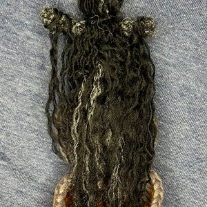 Puede incluir: Una mu&ntilde;eca de crochet con el pelo largo y negro, que lleva una cesta de crochet gris y amarilla.
