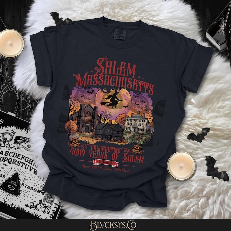 May include: A black t-shirt featuring a graphic print of Salem, Massachusetts. The design includes a witch on a broomstick, a full moon, historic buildings, pumpkins, and bats. Text reads: Salem, Massachusetts, Celebrating 400 Years of Salem 1626-2026.