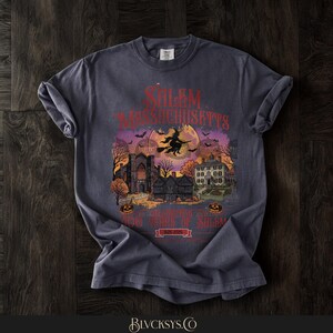 May include: A charcoal gray t-shirt featuring a graphic print of Salem, Massachusetts. The design includes a witch on a broomstick, a full moon, historic buildings, and pumpkins. Text reads Salem Massachusetts, 400 Years of Salem, 1626-2026.