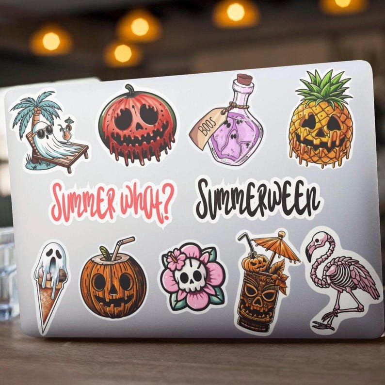 A laptop with various colorful stickers on it. The stickers feature a ghost, a pineapple, a skull, a pumpkin, a potion bottle, a ghost on a beach chair, a cocktail with a skull, a flower with a skull, and a skeleton flamingo. Summer what? Summerween.