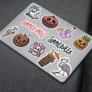 A silver laptop with various colorful stickers on it. The stickers include a ghost, a pineapple, a skull, a potion bottle, a tiki drink, a flamingo, and a pumpkin. The text on the stickers reads 'Summer What?' and 'Summerween'.
