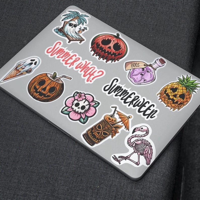 A silver laptop with various colorful stickers on it. The stickers include a ghost, a pineapple, a skull, a potion bottle, a tiki drink, a flamingo, and a pumpkin. The text on the stickers reads 'Summer What?' and 'Summerween'.
