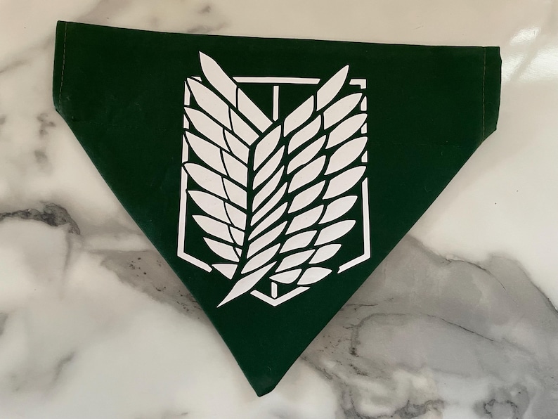 May include: Dark green bandana with a white emblem featuring a stylized wing design inside a geometric frame. The bandana is triangular in shape and made of a smooth fabric. The emblem is centered on the bandana.