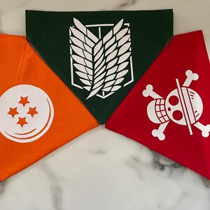 May include: Three triangular bandanas in orange, green, and red. The orange bandana features a white circle with four stars. The green bandana has a white emblem. The red bandana displays a white skull and crossbones design.