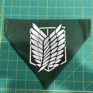May include: A dark green bandana with a white emblem featuring a stylized wing design. The bandana is triangular in shape and made of fabric. The emblem is centered on the bandana.