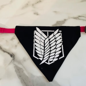 May include: Black dog bandana with a white winged symbol, attached to a pink collar.