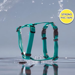 Może przedstawiać: Turkusowy niebieski szelek dla psa z czarnymi klamrami i srebrnymi akcentami. Szelki unoszą się na wodzie z kroplami wody w tle. Tekst "STRONG PVC TAPE" znajduje się w żółtym kółku w prawym górnym rogu obrazu.