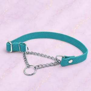 May include: A teal textured collar featuring a silver-toned metal chain attachment. The collar includes an adjustable sliding buckle, a metal loop for the chain, and a single silver snap button closure on the strap to secure the fit around the neck.