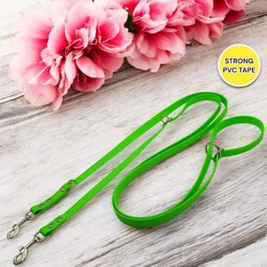 Op de afbeelding: Een groene dubbele hondenriem met twee metalen clips. De riem is gemaakt van sterk PVC-tape.