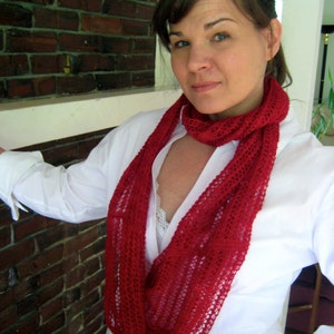 May include: A woman wearing a white shirt with a red crocheted infinity scarf. The scarf is a loose knit with a lacy pattern.