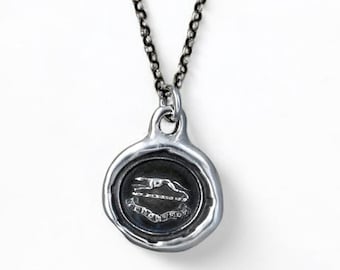 May include: A silver necklace with a round pendant featuring a wax seal design. The seal has a raised image of a bird and the text "Always Remember" around the edge.