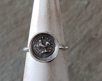 May include: A silver ring with a round, raised design featuring a rooster and the inscription "VIRTUS IN ACTIONE".
