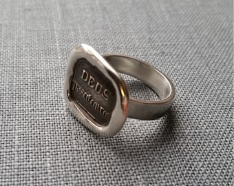 Può includere: Un anello sigillo in argento con una superficie rettangolare rialzata che presenta l'iscrizione "DEUS PASCIT CORVOS".