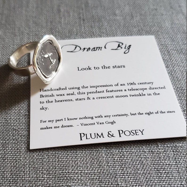 May include: Silver ring with a wax seal pendant featuring a telescope, stars, and a crescent moon. The card reads "Dream Big, Look to the stars" and includes a quote by Vincent Van Gogh: "For my part I know nothing with any certainty, but the sight of the stars makes me dream." The card is signed "Plum & Posey."