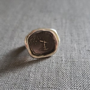 May include: A silver signet ring with a raised design of a tree with a cross on top and stars in the sky. The ring has a textured, irregular shape.