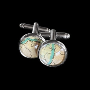 May include: A pair of silver cufflinks with a map design. The round, domed faces feature a vintage map with beige, green, and blue tones. The cufflinks have a classic, elegant design, perfect for adding a touch of sophistication to any outfit.