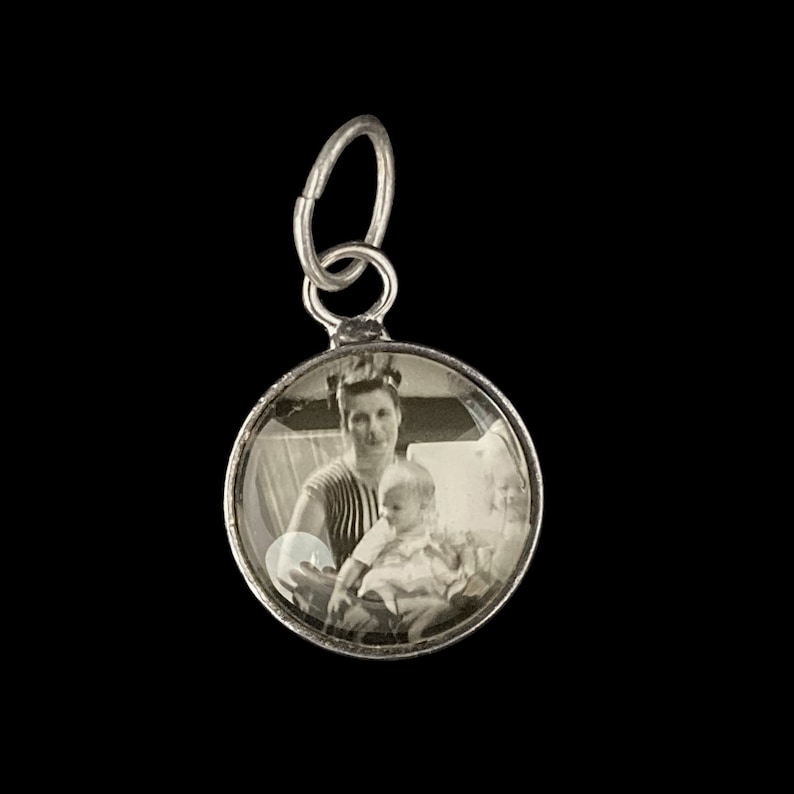 Pu&ograve; includere: Ciondolo in argento con una foto in bianco e nero di una donna che tiene un bambino. Il ciondolo &egrave; rotondo e ha un coperchio in vetro trasparente.