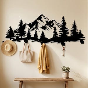 May include: Black metal wall art depicting a mountain range and pine trees. The art piece has hooks for hanging items. A straw hat, tote bag, and jacket hang from the hooks. A wooden bench and potted plant are below.