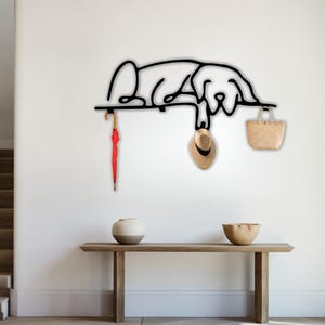 May include: Black metal wall-mounted coat rack shaped like a dog, with a red umbrella, a straw hat, and a straw bag hanging from it.