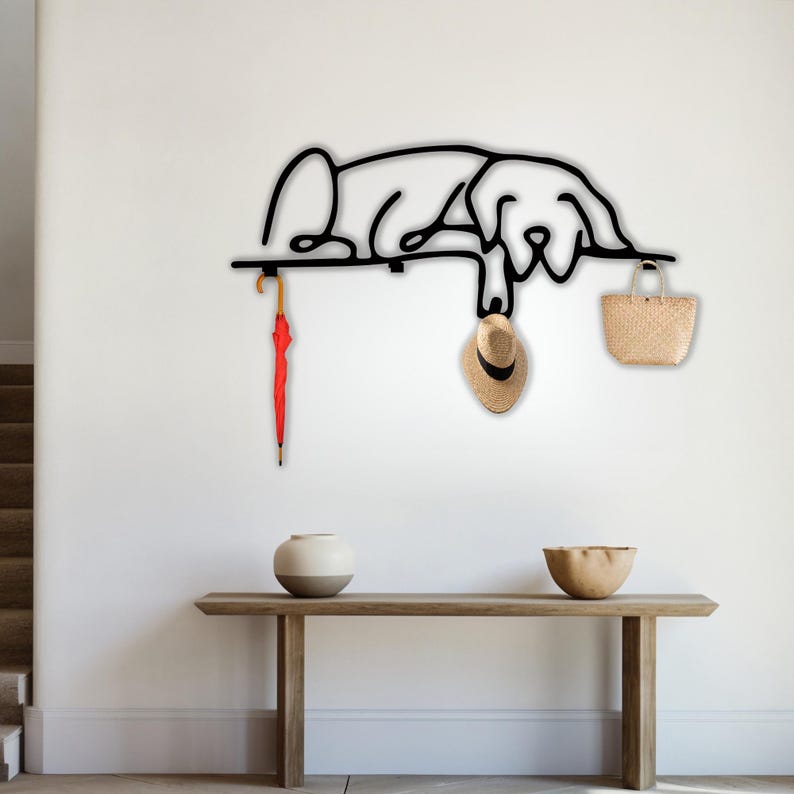 May include: Black metal wall-mounted coat rack shaped like a dog, with a red umbrella, a straw hat, and a straw bag hanging from it.