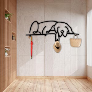 May include: Black metal wall-mounted coat rack shaped like a sleeping dog with a hat and a bag hanging from it.