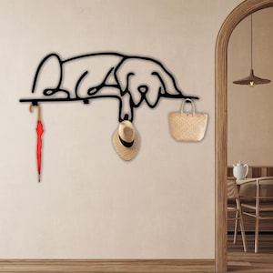 May include: Black metal wall-mounted coat rack shaped like a dog, with a red umbrella, a straw hat, and a straw bag hanging from it.
