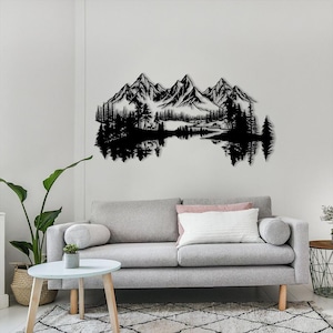 May include: Black metal wall art depicting a mountain range, trees, and a lake. The artwork is mounted on a white wall above a gray sofa. The design features detailed silhouettes of the natural landscape.