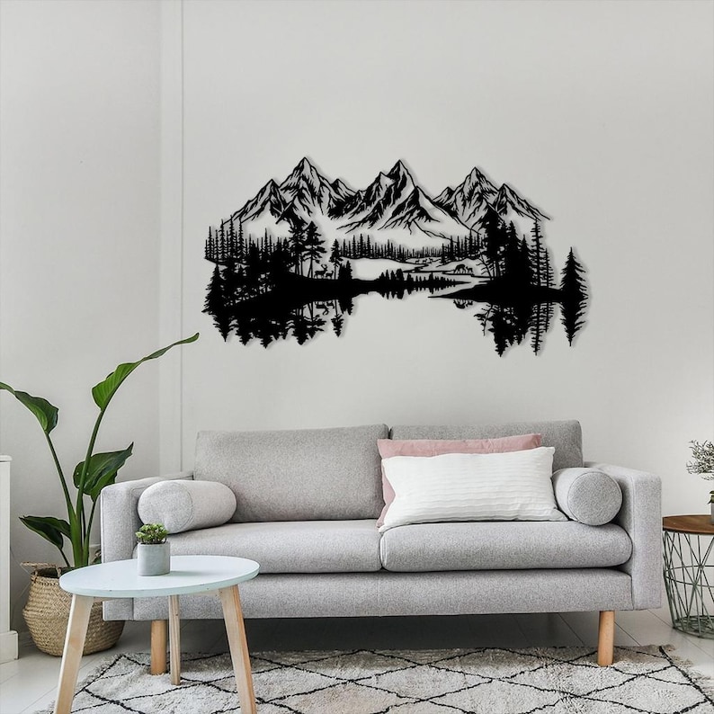May include: Black metal wall art depicting a mountain range, trees, and a lake. The artwork is mounted on a white wall above a gray sofa. The design features detailed silhouettes of the natural landscape.