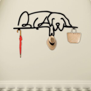 May include: Black metal wall hook shaped like a sleeping dog with a red umbrella, a straw hat, and a woven basket hanging from it.