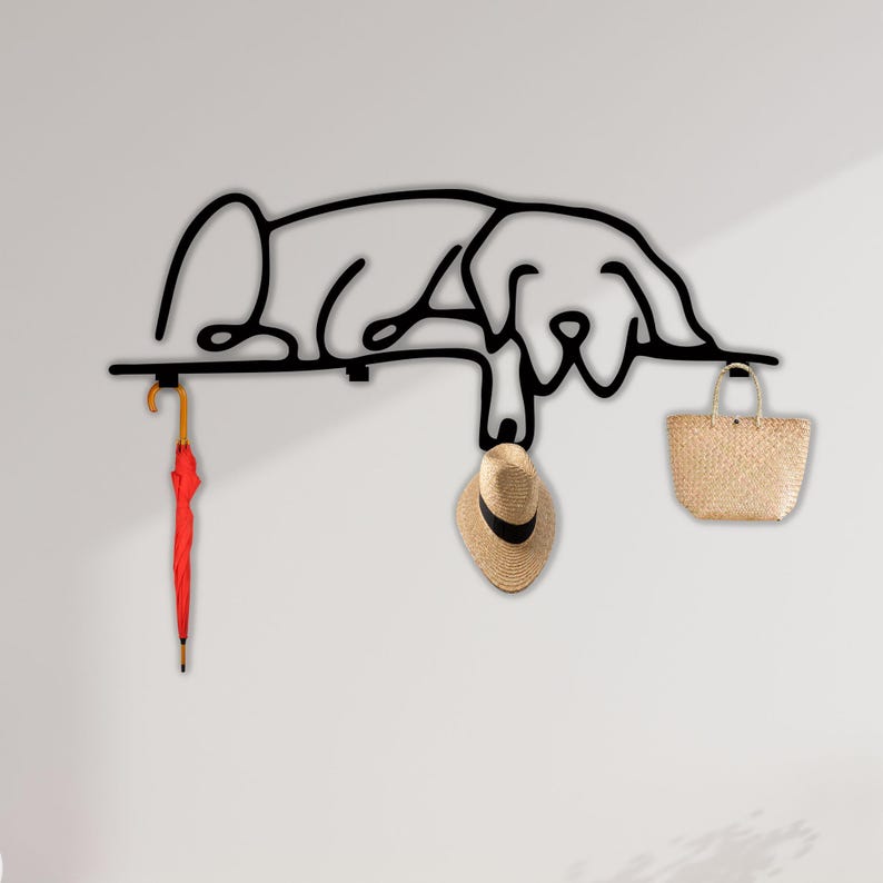 May include: Black metal wall hook shaped like a sleeping dog with a red umbrella, a straw hat, and a woven basket hanging from it.