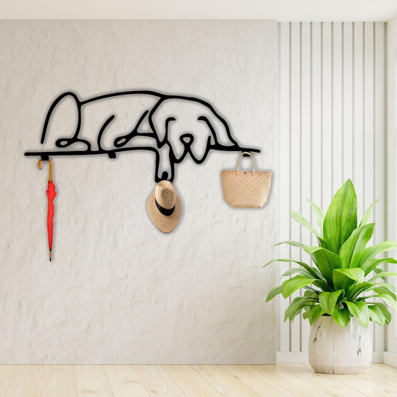 May include: Black metal wall hook shaped like a dog lying down. The hook has a red umbrella, a straw hat, and a woven basket hanging from it.