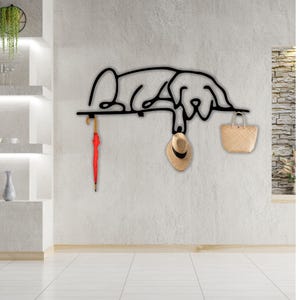 May include: Black metal wall-mounted coat rack shaped like a dog, with a red umbrella hanging from one hook and a straw hat and a woven bag hanging from the other two hooks.