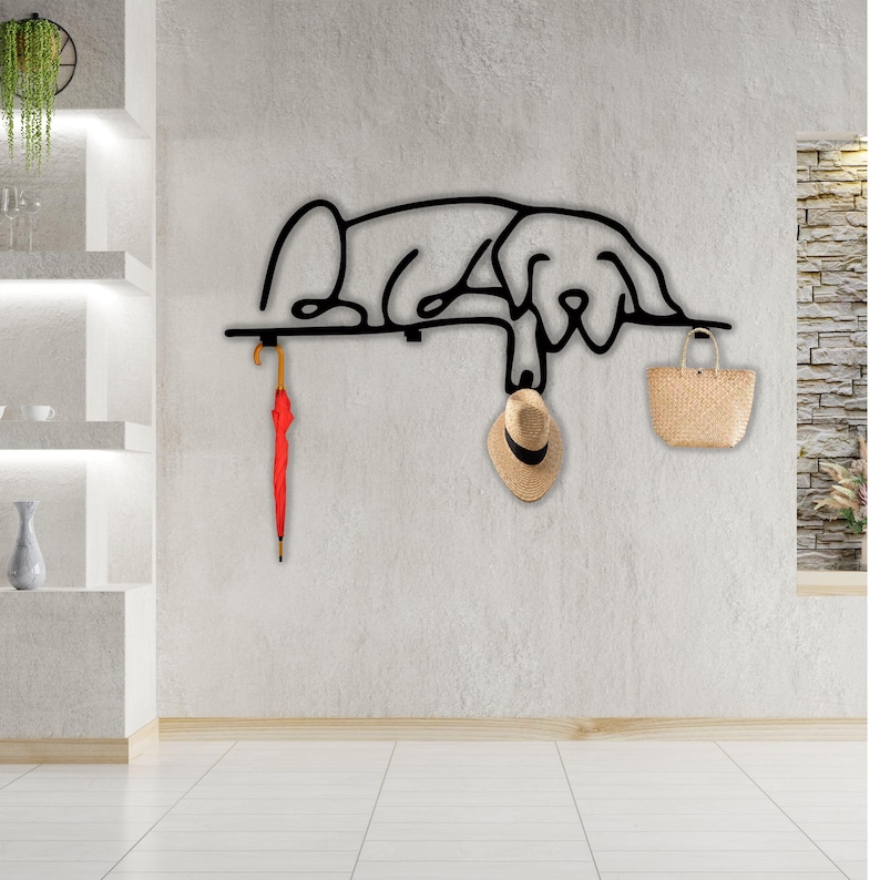 May include: Black metal wall-mounted coat rack shaped like a dog, with a red umbrella hanging from one hook and a straw hat and a woven bag hanging from the other two hooks.