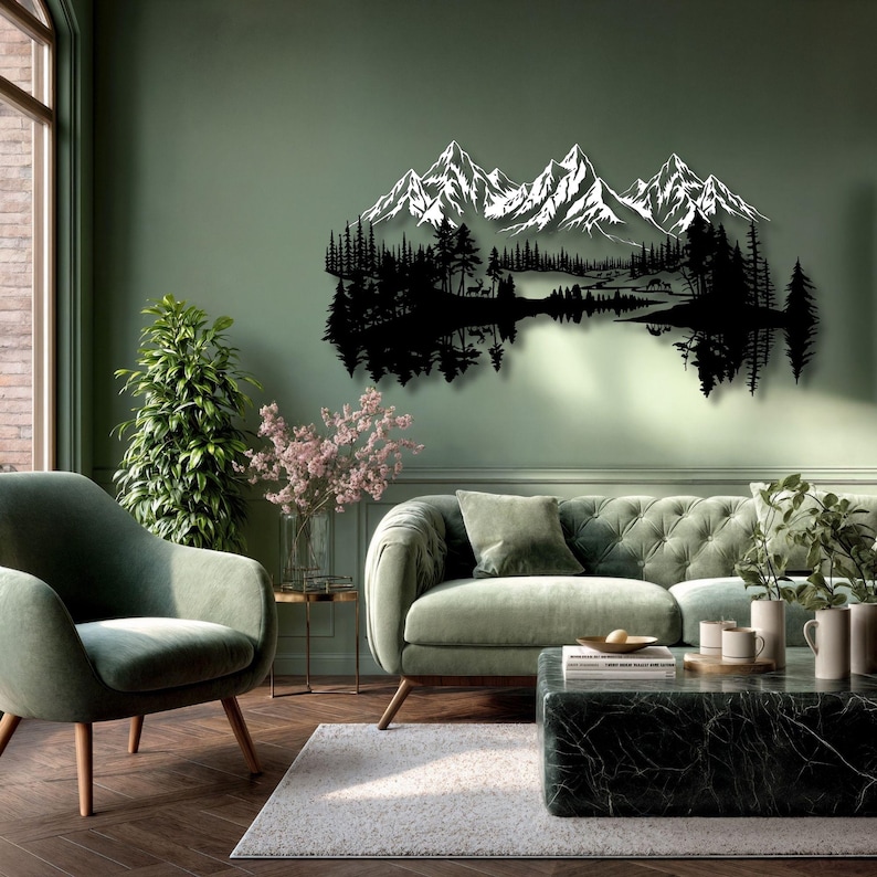 May include: A black metal wall art piece depicting a mountain range with snow-capped peaks, a forest, and a lake. The artwork is mounted on a green wall above a green sofa and chair. The room has a modern, minimalist design with natural light.